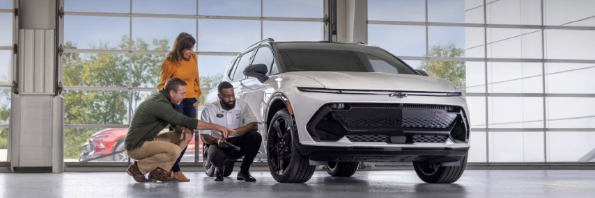 Chevrolet service technician reviewing a clipboard with a man and woman next to a white SUV inside a service bay.